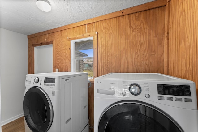 washroom featuring separate washer and dryer, hardwood / wood-style flooring, wooden walls, and a textured ceiling