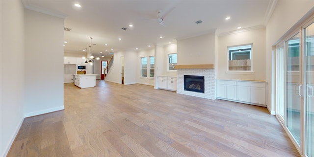 unfurnished living room with ceiling fan, light wood-type flooring, ornamental molding, and a fireplace