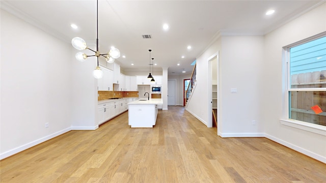 kitchen with a kitchen island with sink, ornamental molding, built in microwave, decorative light fixtures, and white cabinetry