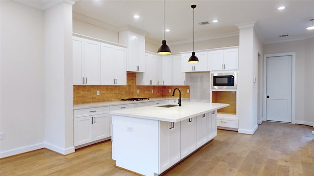 kitchen featuring tasteful backsplash, built in microwave, a kitchen island with sink, sink, and white cabinetry