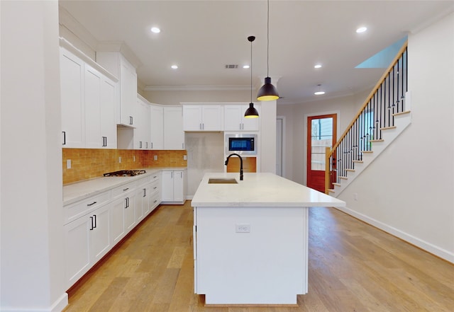 kitchen with a center island with sink, sink, hanging light fixtures, built in microwave, and white cabinetry