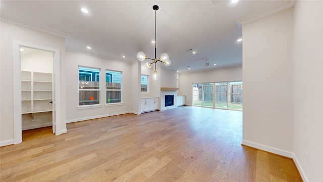 unfurnished living room featuring a chandelier, light hardwood / wood-style floors, crown molding, and a brick fireplace