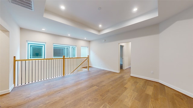 spare room with a raised ceiling and light hardwood / wood-style flooring