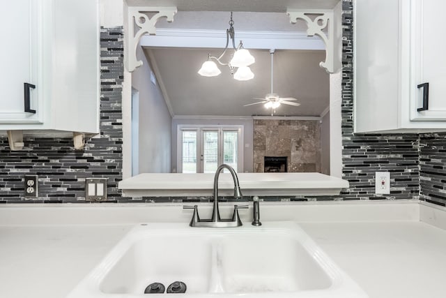 kitchen with white cabinets, ceiling fan with notable chandelier, sink, crown molding, and a premium fireplace