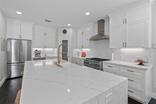 kitchen with white cabinetry, wall chimney range hood, premium appliances, tasteful backsplash, and light stone counters