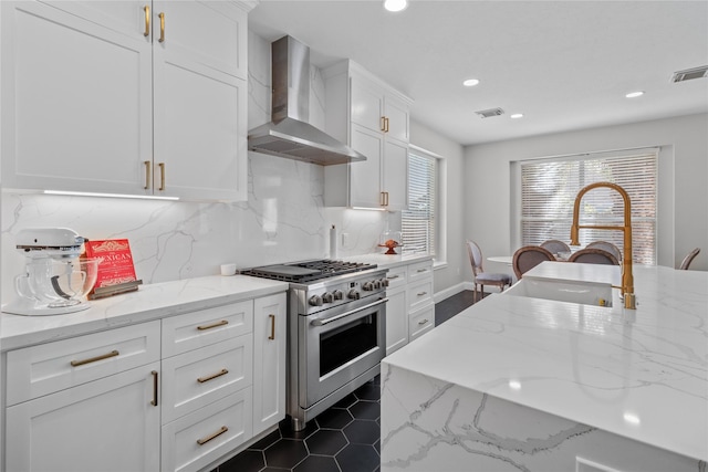 kitchen featuring white cabinetry, light stone countertops, wall chimney range hood, and stainless steel range