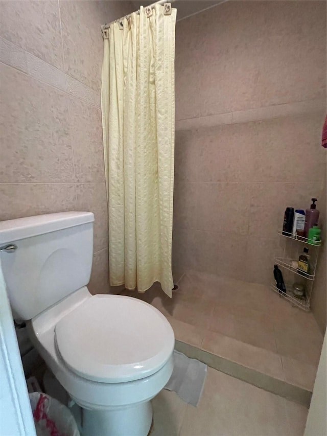 bathroom with toilet, tile patterned floors, curtained shower, and tile walls