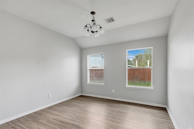 spare room featuring a chandelier, vaulted ceiling, and wood-type flooring