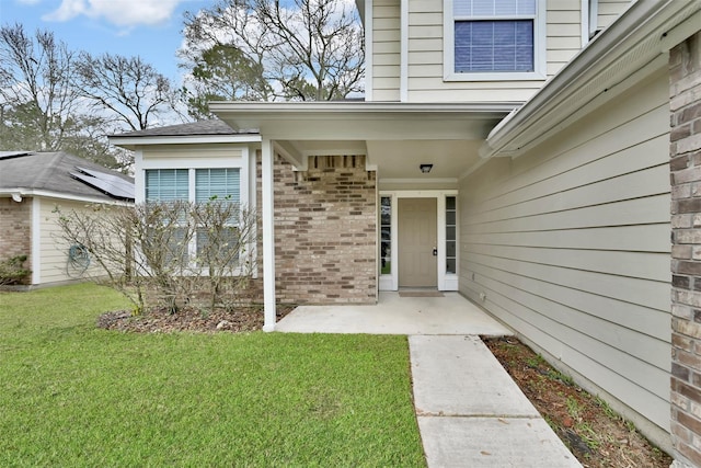 view of exterior entry with a lawn and a patio