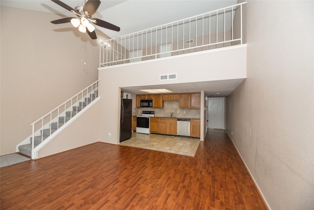 unfurnished living room with a towering ceiling, ceiling fan, dark wood-type flooring, and sink