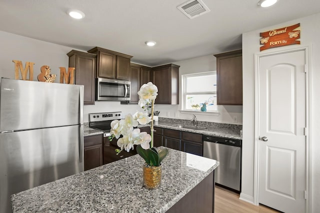 kitchen featuring light stone countertops, dark brown cabinets, stainless steel appliances, sink, and a kitchen island