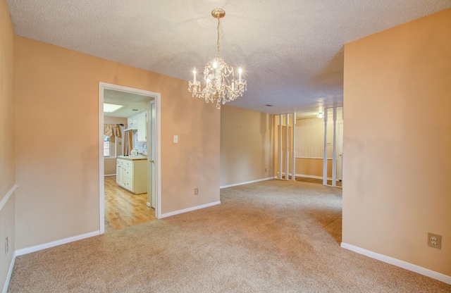 spare room featuring a chandelier, light colored carpet, and a textured ceiling