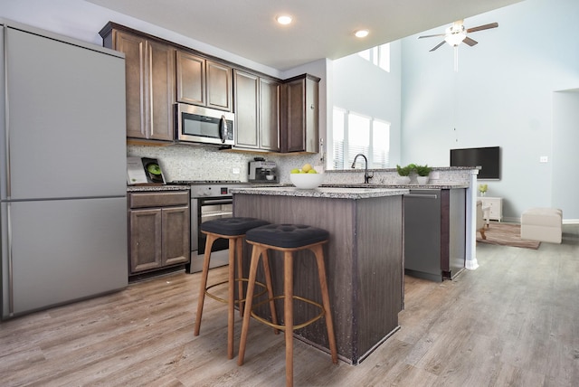 kitchen with dark brown cabinetry, sink, a center island, light hardwood / wood-style floors, and appliances with stainless steel finishes