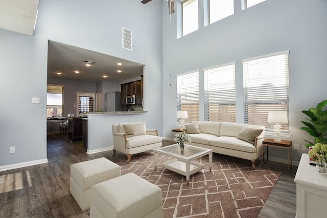 living room with ceiling fan, dark hardwood / wood-style flooring, and a towering ceiling