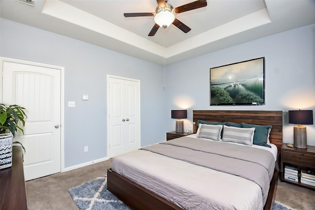 carpeted bedroom with a tray ceiling, ceiling fan, and a closet