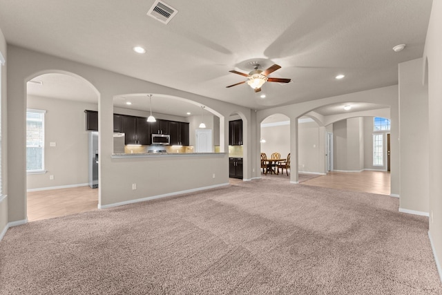 unfurnished living room with light colored carpet and ceiling fan