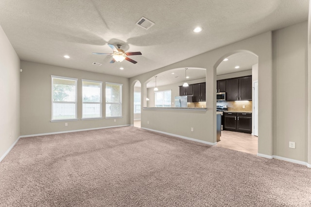 unfurnished living room with light carpet, ceiling fan, and a textured ceiling