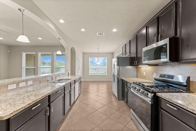 kitchen with sink, light stone countertops, light tile patterned floors, decorative light fixtures, and stainless steel appliances