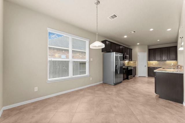 kitchen featuring light stone countertops, tasteful backsplash, dark brown cabinetry, stainless steel appliances, and hanging light fixtures