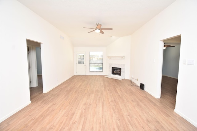 unfurnished living room with ceiling fan, vaulted ceiling, a tile fireplace, and light hardwood / wood-style flooring