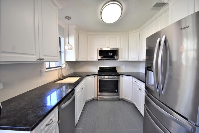 kitchen featuring dark stone counters, stainless steel appliances, sink, white cabinetry, and hanging light fixtures