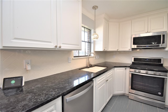 kitchen featuring stainless steel appliances, sink, pendant lighting, dark stone countertops, and white cabinets