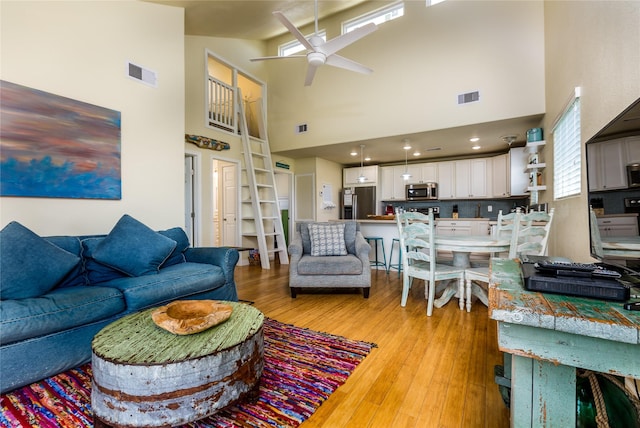 living room featuring ceiling fan, light hardwood / wood-style floors, and a towering ceiling