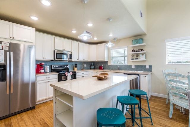 kitchen featuring white cabinets, sink, appliances with stainless steel finishes, decorative light fixtures, and light hardwood / wood-style floors