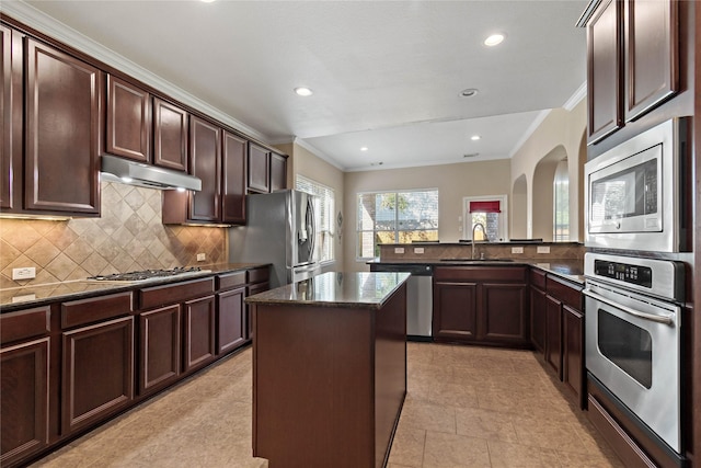 kitchen with kitchen peninsula, appliances with stainless steel finishes, backsplash, dark stone counters, and a kitchen island