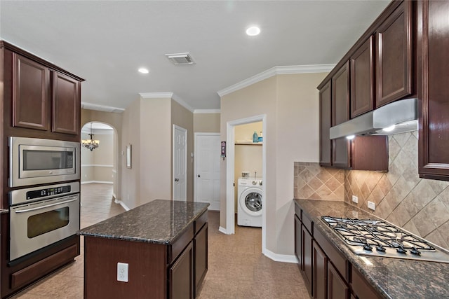 kitchen with dark stone countertops, ornamental molding, appliances with stainless steel finishes, a kitchen island, and washer / clothes dryer