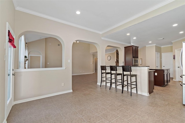 kitchen featuring a breakfast bar, stainless steel microwave, ornamental molding, an island with sink, and dark brown cabinetry