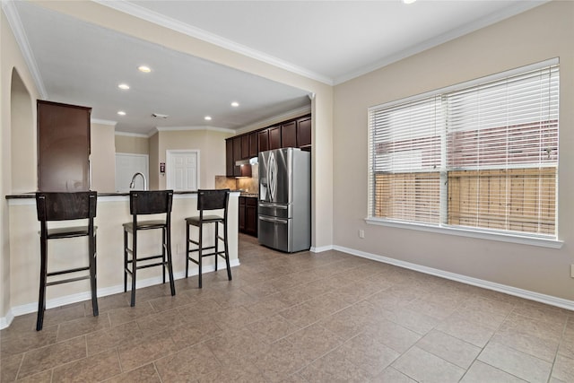 kitchen with dark brown cabinetry, a kitchen breakfast bar, stainless steel fridge, a kitchen island with sink, and ornamental molding