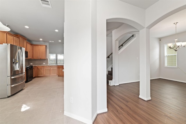 kitchen featuring pendant lighting, an inviting chandelier, black range, stainless steel fridge, and tasteful backsplash