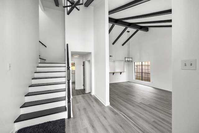 staircase with beam ceiling, hardwood / wood-style flooring, and high vaulted ceiling