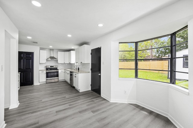 kitchen with decorative backsplash, appliances with stainless steel finishes, sink, wall chimney range hood, and white cabinetry