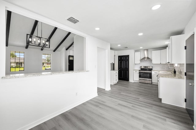 kitchen with stainless steel electric stove, kitchen peninsula, vaulted ceiling with beams, wall chimney exhaust hood, and white cabinetry