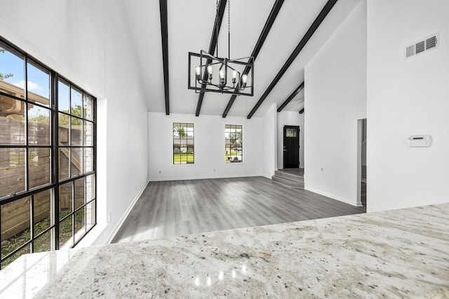 unfurnished living room with vaulted ceiling with beams, hardwood / wood-style flooring, and a notable chandelier