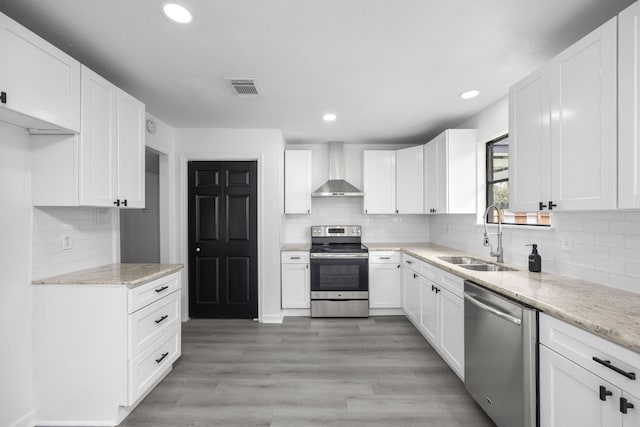 kitchen featuring white cabinetry, sink, wall chimney exhaust hood, stainless steel appliances, and light stone counters