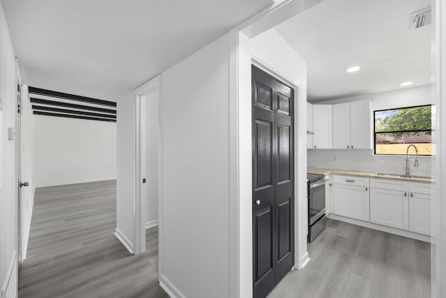 kitchen featuring light wood-type flooring, tasteful backsplash, stainless steel electric stove, sink, and white cabinetry