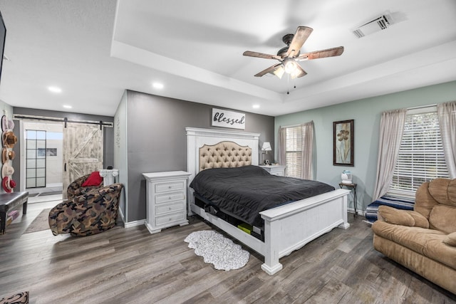 bedroom with ceiling fan, a barn door, a raised ceiling, and dark wood-type flooring