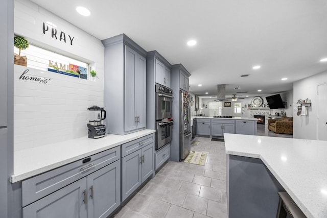 kitchen featuring ceiling fan, gray cabinets, light stone counters, island exhaust hood, and stainless steel appliances