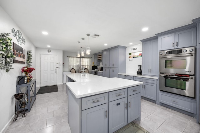 kitchen featuring gray cabinetry, double oven, an island with sink, pendant lighting, and light tile patterned floors