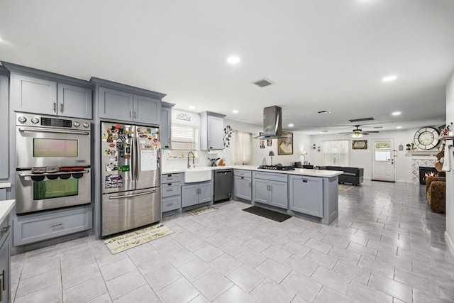 kitchen with ceiling fan, sink, kitchen peninsula, island range hood, and appliances with stainless steel finishes