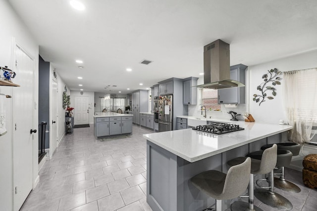 kitchen with island exhaust hood, kitchen peninsula, gray cabinetry, and appliances with stainless steel finishes