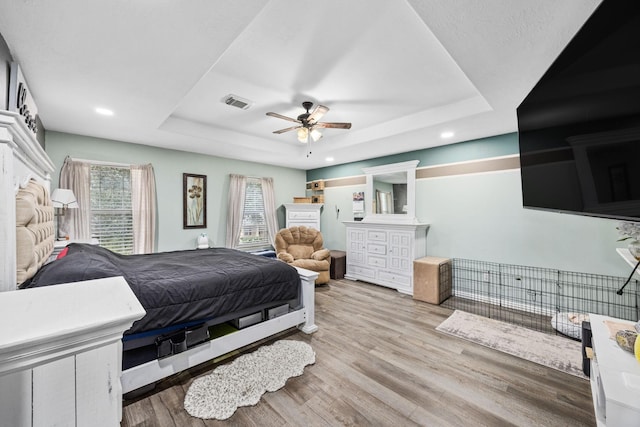 bedroom with ceiling fan, a raised ceiling, and light wood-type flooring