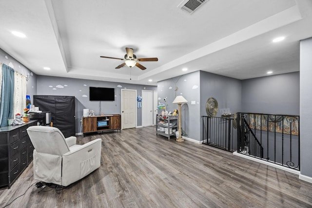 living room featuring a tray ceiling, ceiling fan, and wood-type flooring