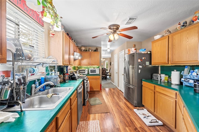 kitchen featuring sink, ceiling fan, a textured ceiling, appliances with stainless steel finishes, and light hardwood / wood-style floors