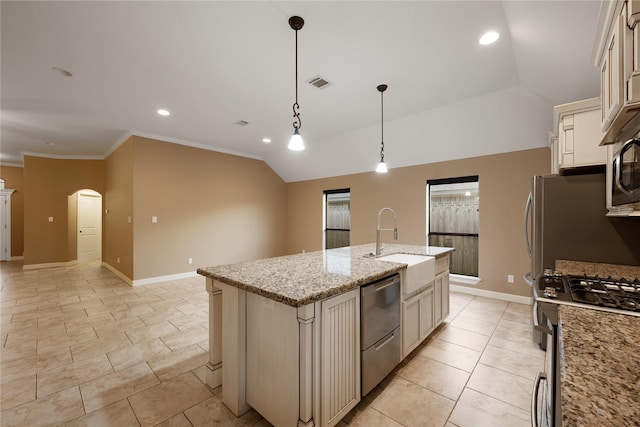 kitchen featuring stainless steel appliances, light stone counters, cream cabinets, pendant lighting, and a kitchen island with sink