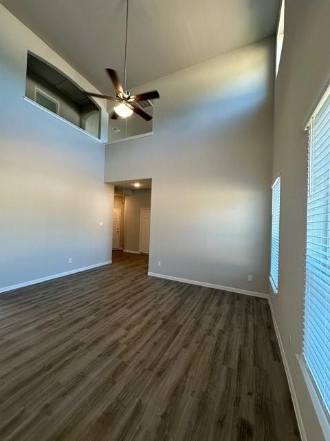 empty room featuring dark hardwood / wood-style floors, ceiling fan, and a towering ceiling