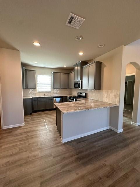 kitchen with kitchen peninsula, appliances with stainless steel finishes, backsplash, hardwood / wood-style floors, and gray cabinets